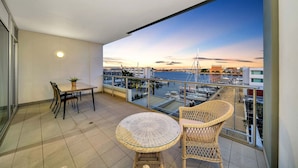 Un balcon avec une table et des chaises, donnant sur une marina où l’on peut admirer des bateaux et des bâtiments.