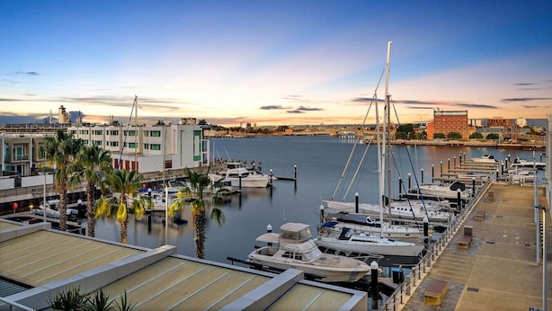 Un port de plaisance avec des bateaux amarrés, un bâtiment doté d’un toit plat et un ciel dégagé.