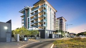 Un immeuble résidentiel à plusieurs étages, doté de balcons, d’une entrée sécurisée et d’un espace paysager agrémenté d’arbustes.