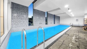Une longue piscine intérieure à l’eau bleue, dotée de rampes métalliques et d’un mur à texture sur l’un des côtés.