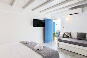 A modern hotel room with a bed, a sofa, a TV, and a blue door.