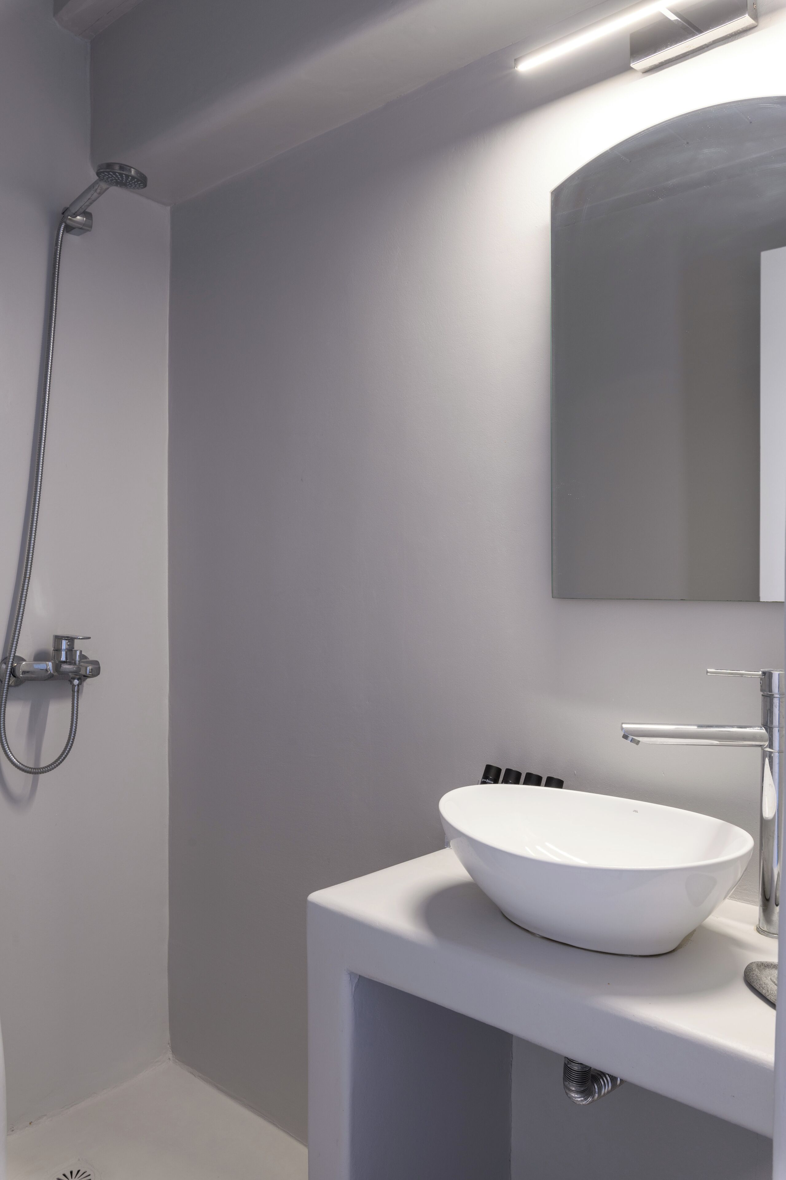 Un baño moderno con un lavamanos blanco, un espejo grande y un cabezal de ducha.
