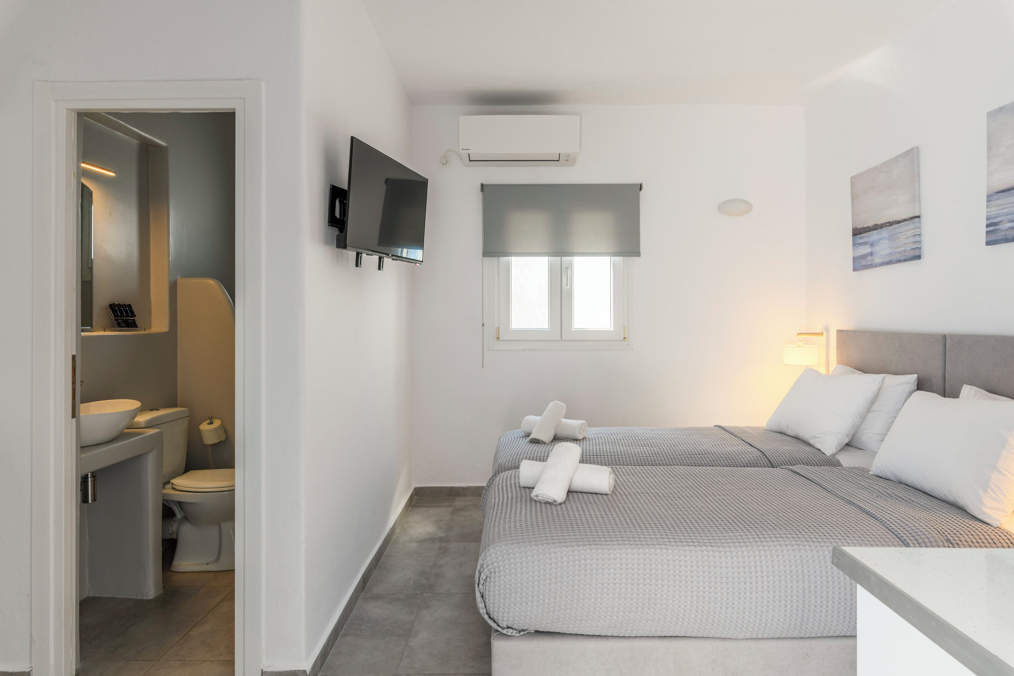 Une chambre d’hôtel de taille réduite, comprenant un lit, deux tables de chevet, un téléviseur, un appareil de climatisation et une fenêtre donnant sur un paysage agréable.