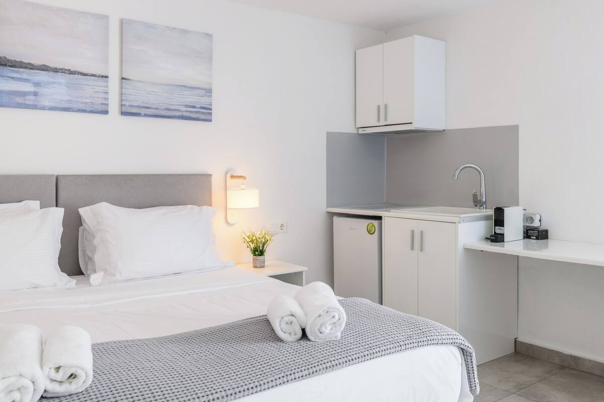 A hotel room with a bed, a small desk, a kitchenette, and a wall-mounted cabinet.