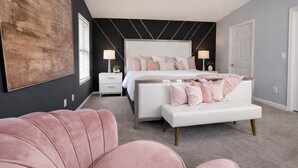 A bedroom with a large bed, bedside tables, a white bench, and a large abstract painting on the wall.