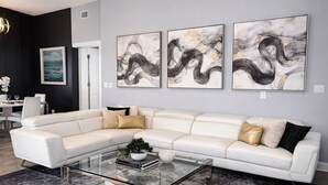 A modern living room with a white sectional sofa, a glass coffee table, and abstract wall art.