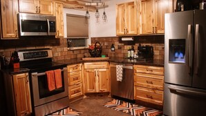 A kitchen with wooden cabinets, stainless steel appliances, and a patterned rug. - Cozy 3-bedroom cabin in charming North East (North East)