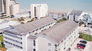 Een meerlaags hotel met een plat dak, verschillende balkons en een parkeerplaats met auto's.