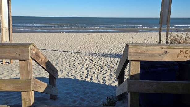 Een houten terras loopt naar een zandstrand, met een helder uitzicht op de oceaan.