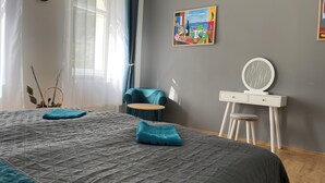 Um quarto com uma cama grande, uma mesa redonda pequena, uma cadeira, uma cômoda com espelho e um quadro na parede.