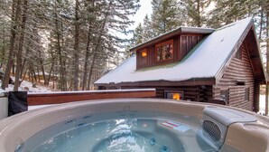 A hot tub in a forested area with a wooden cabin in the background.