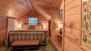 A cozy wooden cabin bedroom with a bed, bench, and a framed botanical print on the wall.