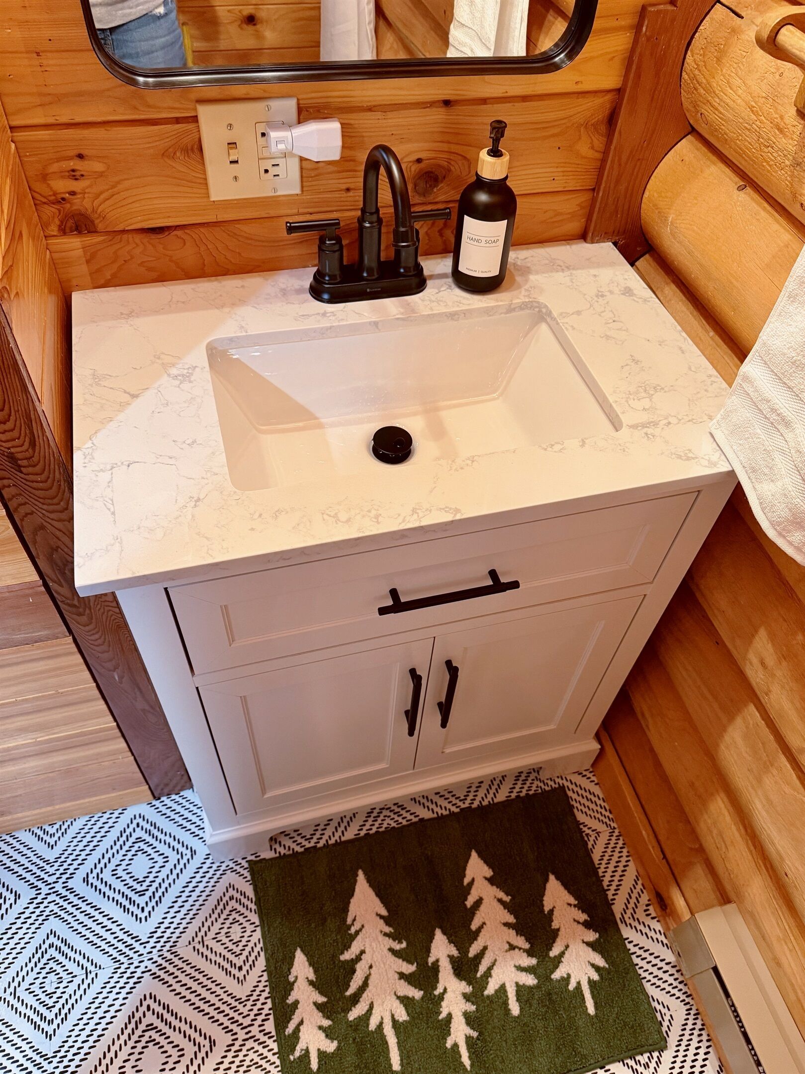 Une salle de bain avec un lavabo blanc, des murs en bois, un miroir et un flacon de savon pour les mains.