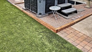 A backyard with a stone hot tub, two small tables, and a wooden deck. - Hot Tub, King Beds, Pet Friendly Close to I25 (Fountain)
