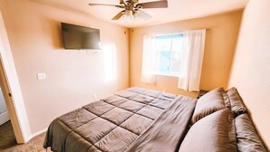 A bedroom with a bed, ceiling fan, window with curtains, and a flat-screen TV mounted on the wall. - Hot Tub, King Beds, Pet Friendly Close to I25 (Fountain)