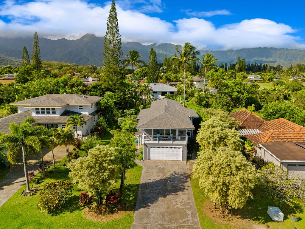 A residential area with houses surrounded by lush greenery and mountains in the background.