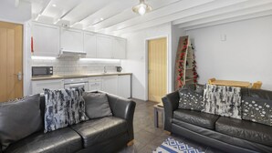 A modern living room with a black leather sofa, a small side table, and a patterned rug. - Fisherman's Nook - North East Escapes (Seahouses)