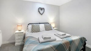 A neatly made bed with a plaid bedspread, two bedside lamps, and a heart-shaped decoration on the wall. - Fisherman's Nook - North East Escapes (Seahouses)