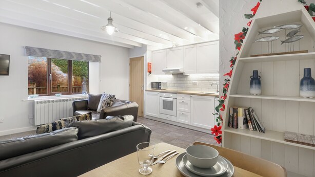 A modern living room with a sofa, dining table, and kitchen in the background. - Fisherman's Nook - North East Escapes (Seahouses)