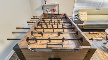 A foosball table in a room with a sofa and a small shelf with toys.