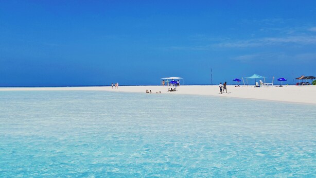 A beach with clear blue water and white sand. There are umbrellas and people on the beach.