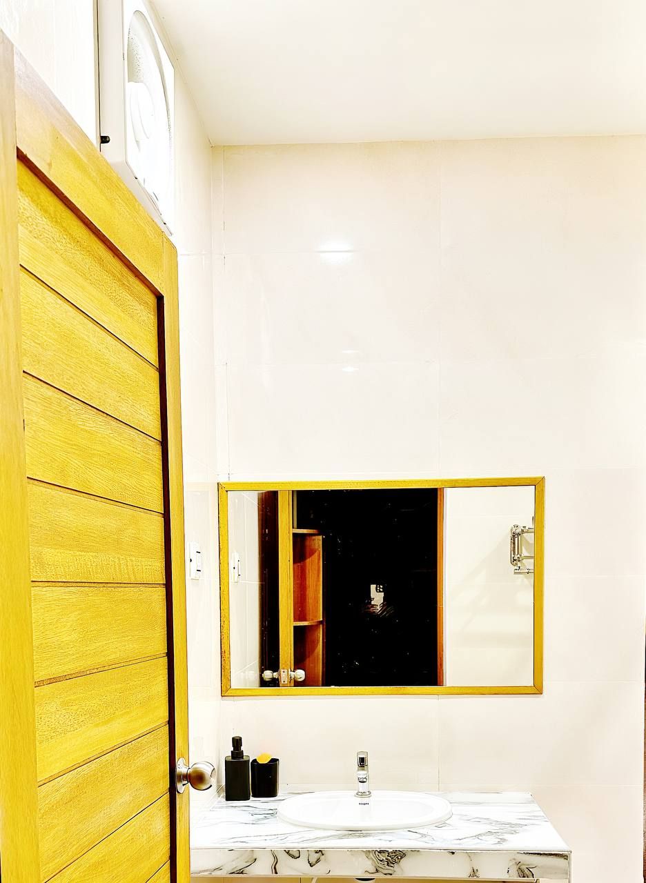 Un baño con una puerta amarilla, un lavamanos blanco y un espejo con marco dorado.