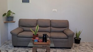 A living room with a sofa, a coffee table with a tray of snacks, two potted plants, and three framed pictures on the wall.