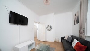 Ett modernt vardagsrum med en platt-TV, ett soffbord i glas, en svart lädersoffa och en vit mediabänk.