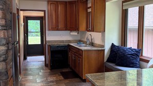 A kitchen with wooden cabinets, a granite countertop, and a stone-tiled floor. - Charming Lake House! (Wild Rose)