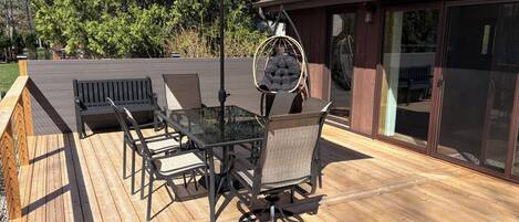Una terraza con una mesa de vidrio, sillas y una mecedora colgante.