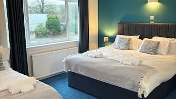 A hotel room with a large bed, a smaller bed, a window with curtains, a wall-mounted light, and a view of the outside.