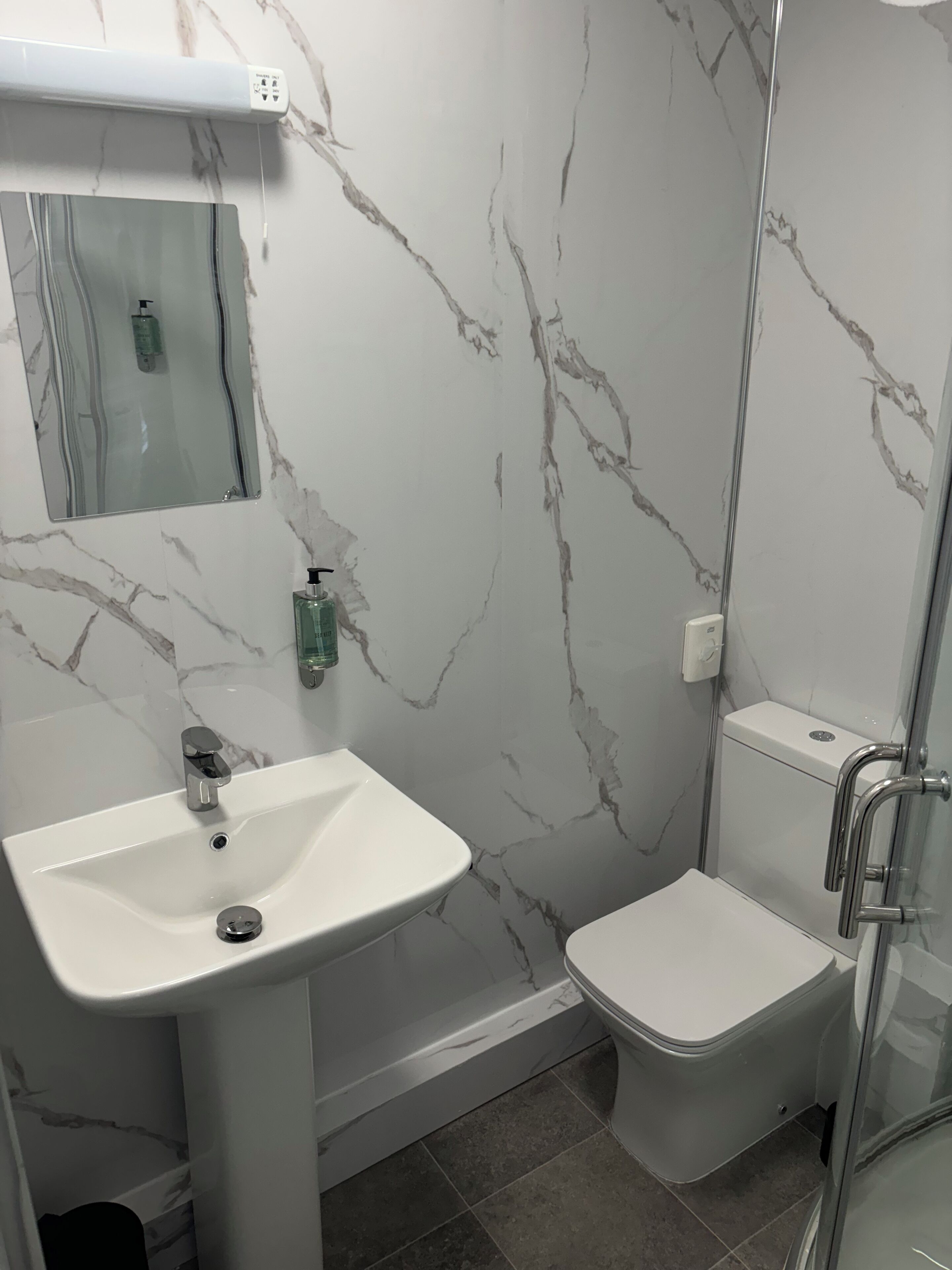 Une salle de bain avec un lavabo blanc, un miroir, des toilettes et un espace douche.