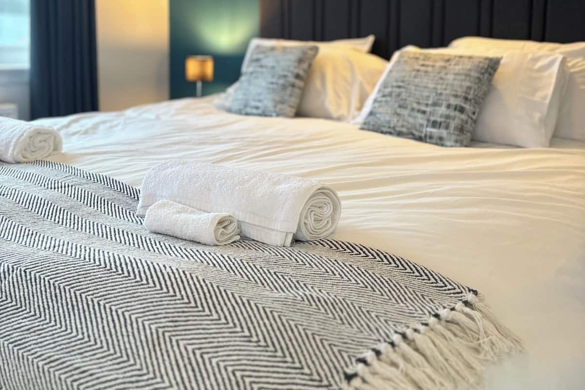 Ein ordentlich gemachtes Bett mit aufgerollten weißen Handtüchern, einer gemusterten Tagesdecke und zwei Kissen.