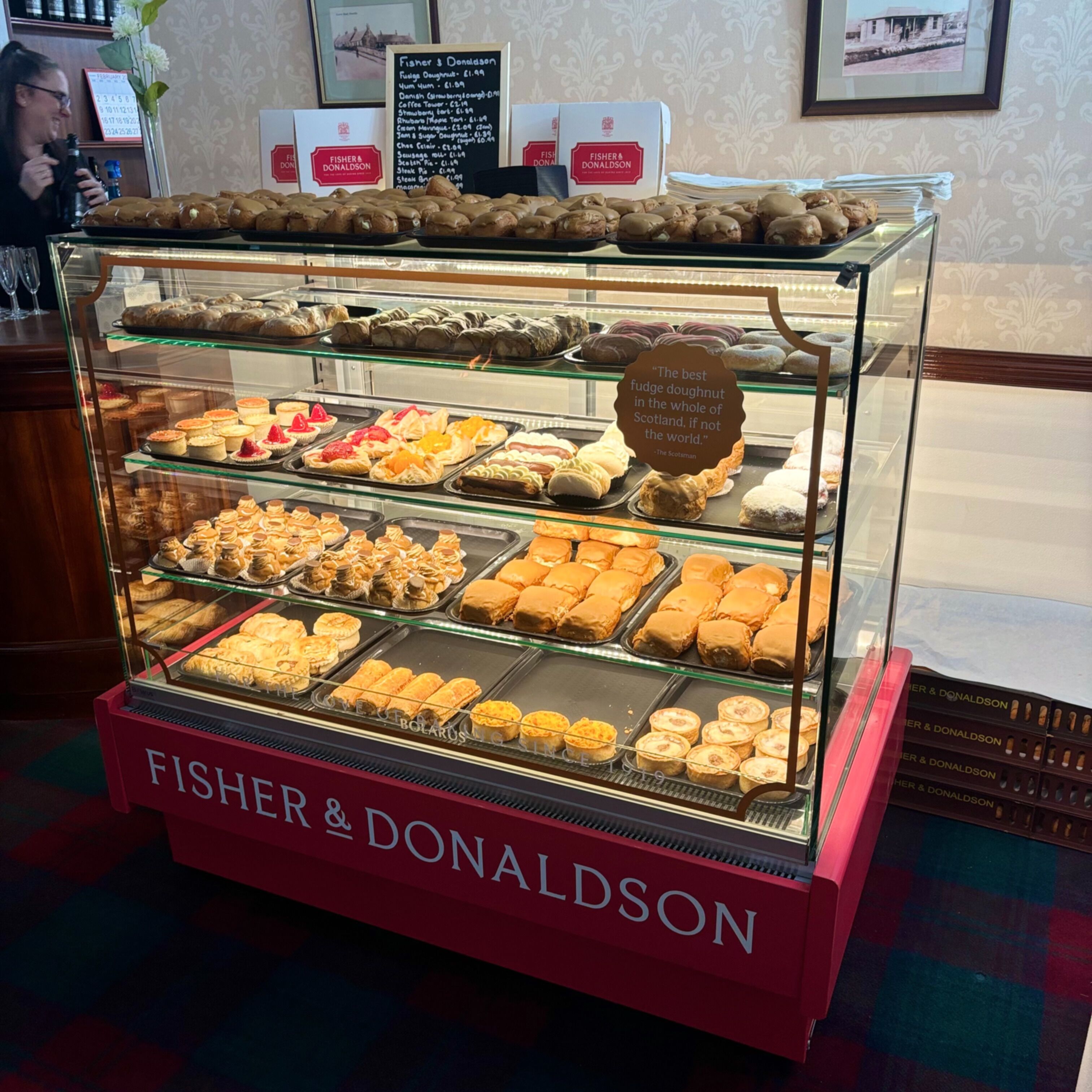 A bakery display case with various pastries and a sign stating "The best fudge doughnut in the whole of Scotland, if not the world."