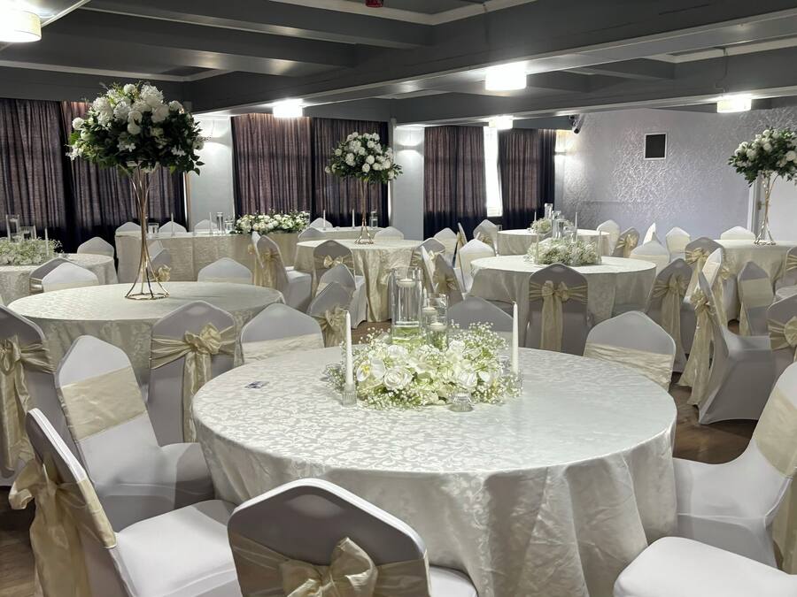 A banquet hall with round tables, white chairs with gold sashes, and floral centerpieces.