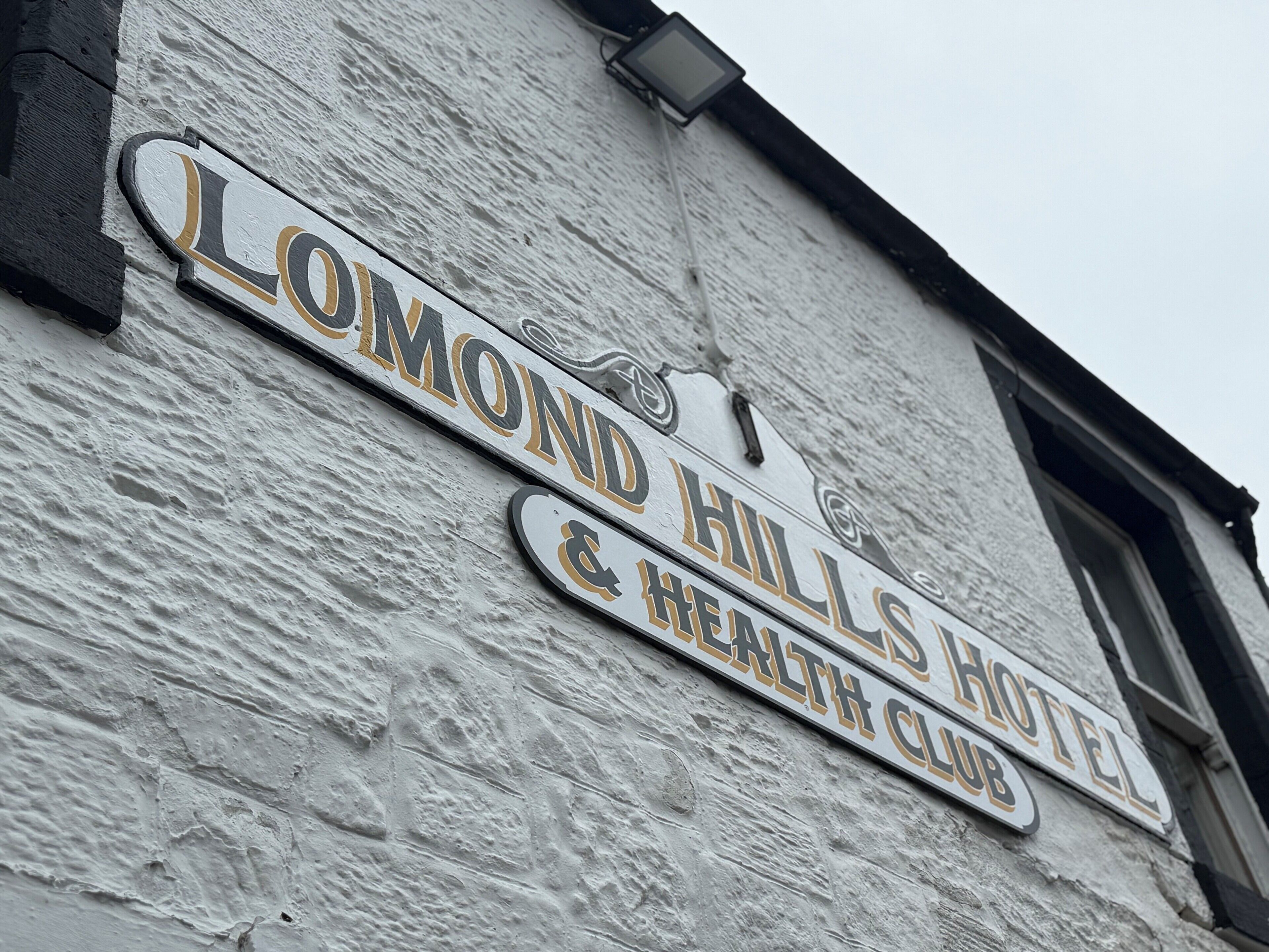 Placa com o nome 'Lomond Hills Hotel & Health Club' em fachada de um edifício com textura.