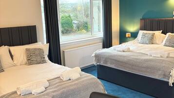 A hotel room with two beds, a view of greenery outside, and a blue carpet.