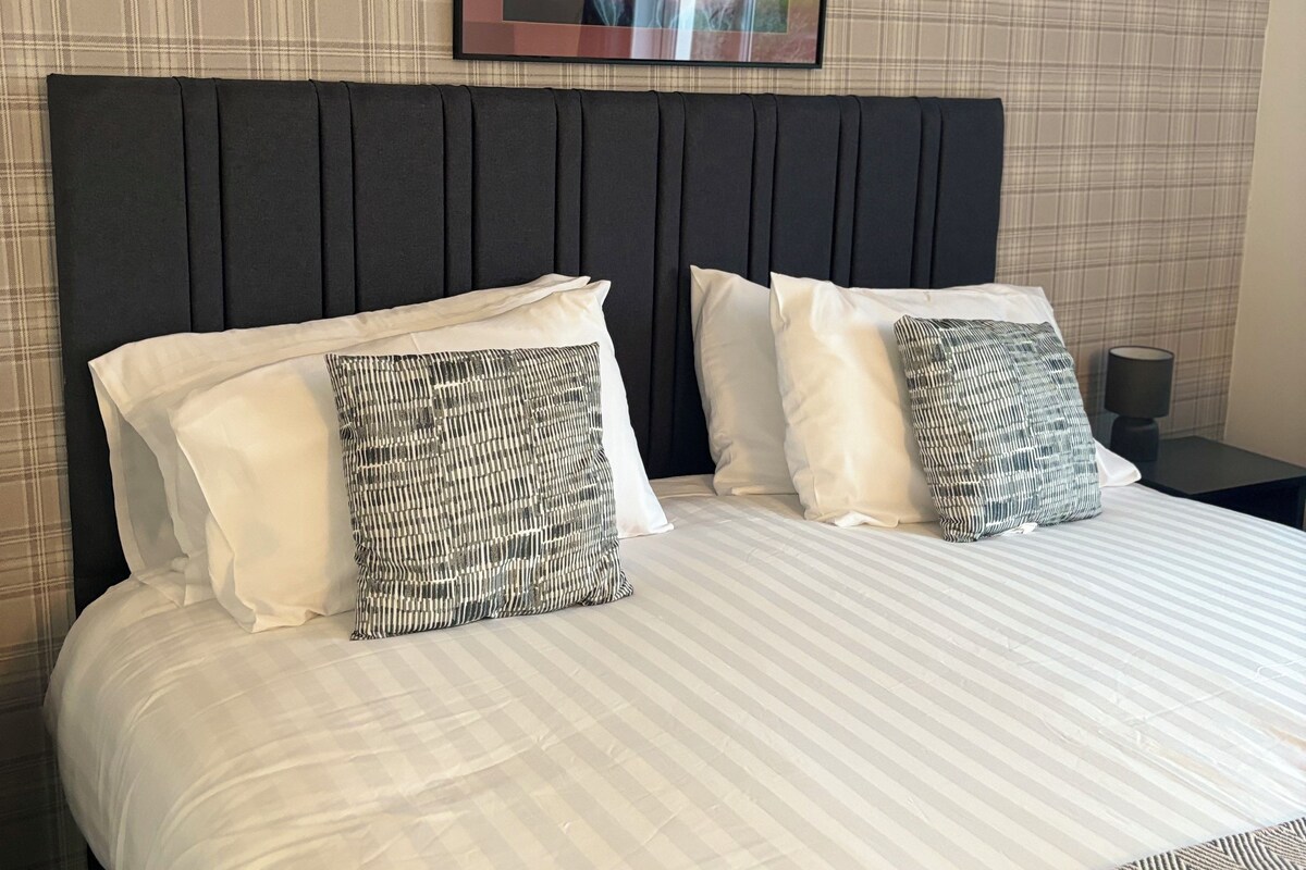 A double bed with a dark headboard, two white pillows, and two patterned pillows.