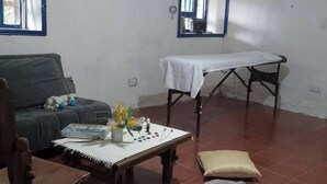 A room with a sofa, a small table with a white cloth, a wooden chair, and a bed with pillows. - Room in Casa de Campo via the airport (Copacabana)