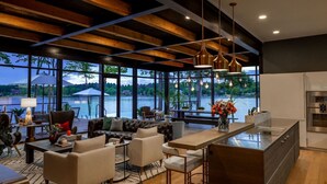 A modern kitchen with a large island, a dining area with a view of a lake, and a cozy seating area with a fireplace. - NEW! 151 House on Lake Oconee (Eatonton)