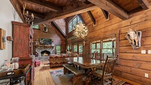 A rustic wooden cabin interior with a stone fireplace, wooden dining table, benches, and various hunting trophies.