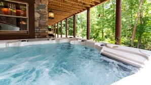 A hot tub with a stone wall and wooden ceiling, surrounded by greenery.