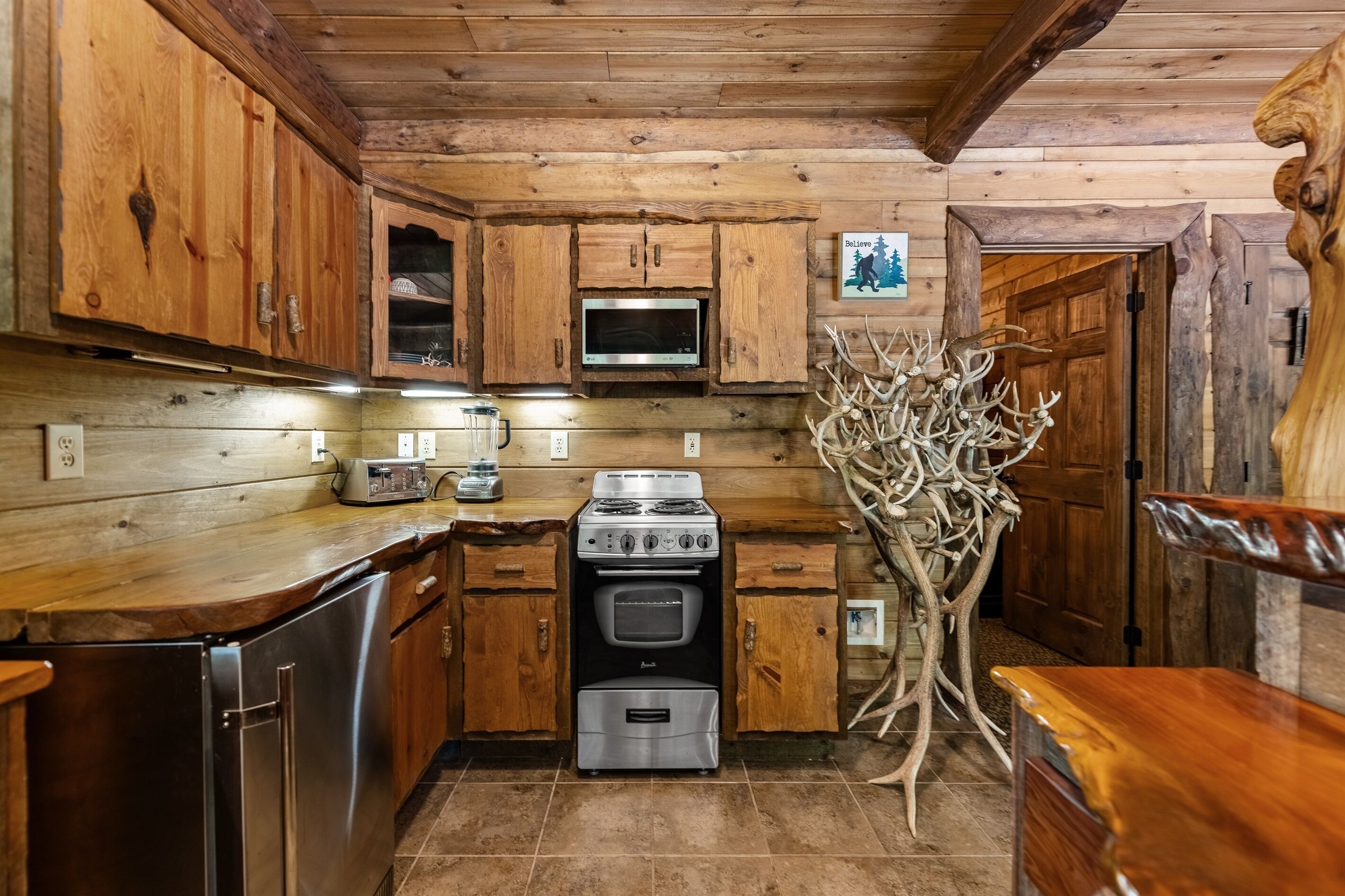 A wooden cabin kitchen with a stove, oven, microwave, and wooden cabinets.