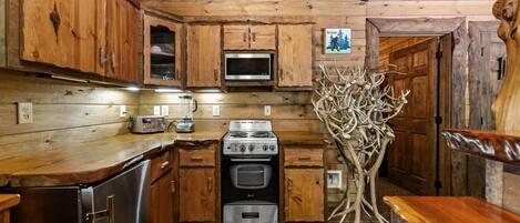 A wooden cabin kitchen with a stove, oven, microwave, and wooden cabinets.