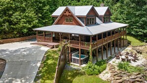 A large wooden cabin with a covered porch, a hot tub, and a stone fire pit area.