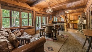A rustic cabin interior with a leather couch, wooden dining table, and a bar area.