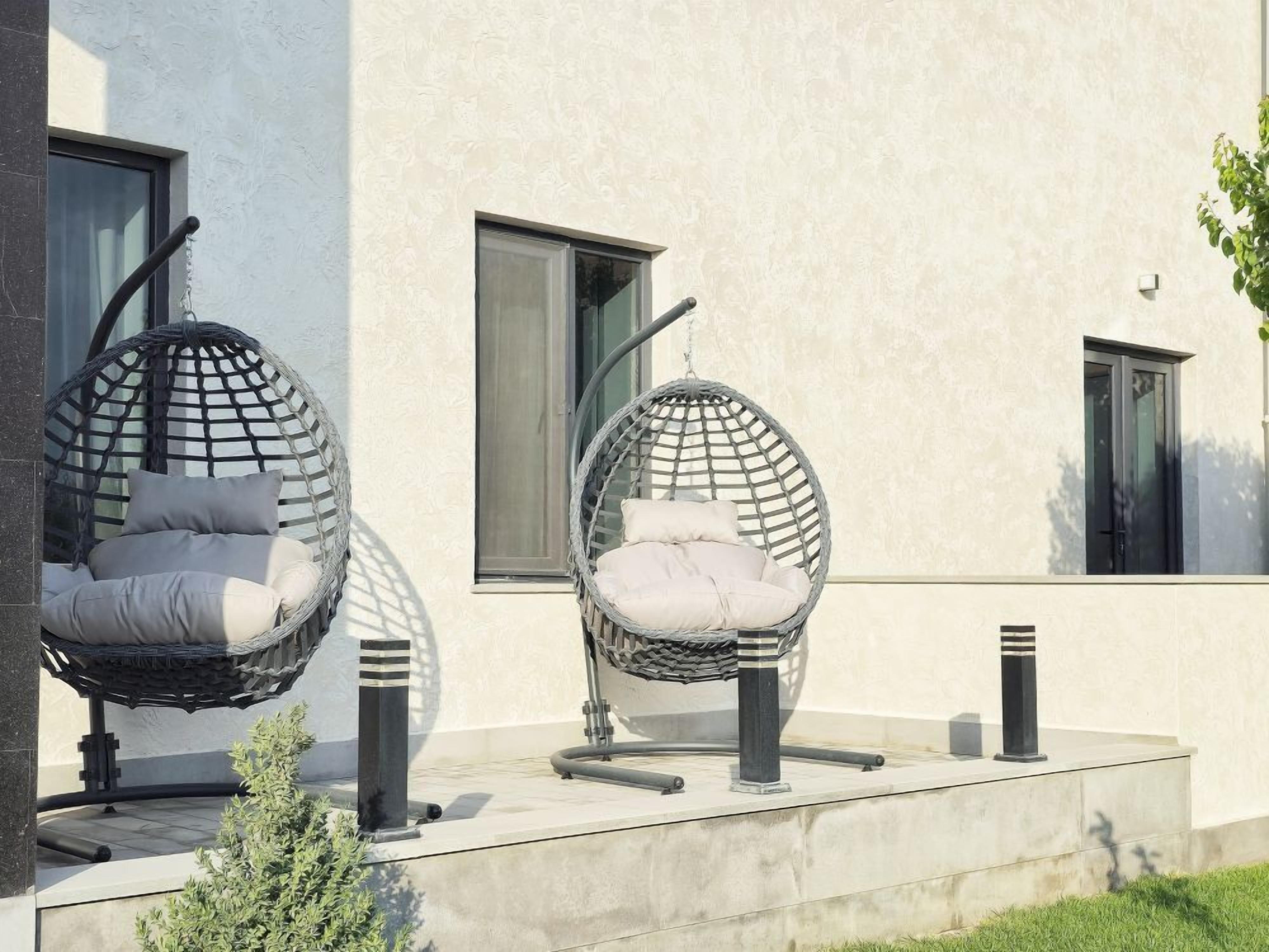 Two hanging chairs with cushions outside a modern building with large windows and a concrete floor.