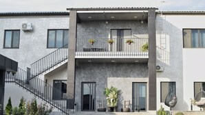 A modern two-story building with a concrete facade, a staircase leading to the entrance, and outdoor seating with potted plants.