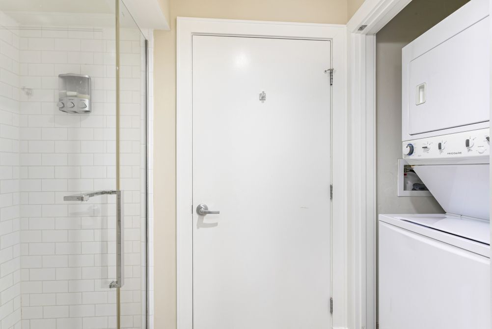Ett badrum med en duschkabin i glas, en vit dörr och en inbyggd tvättmaskin.
