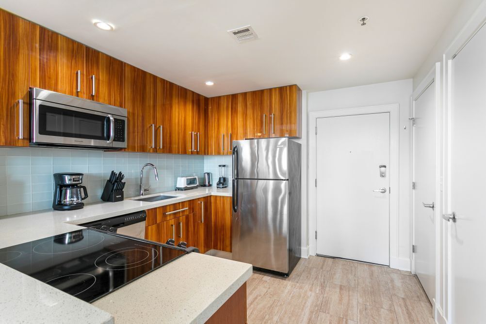 A modern kitchen with wooden cabinets, stainless steel appliances, and a white door.